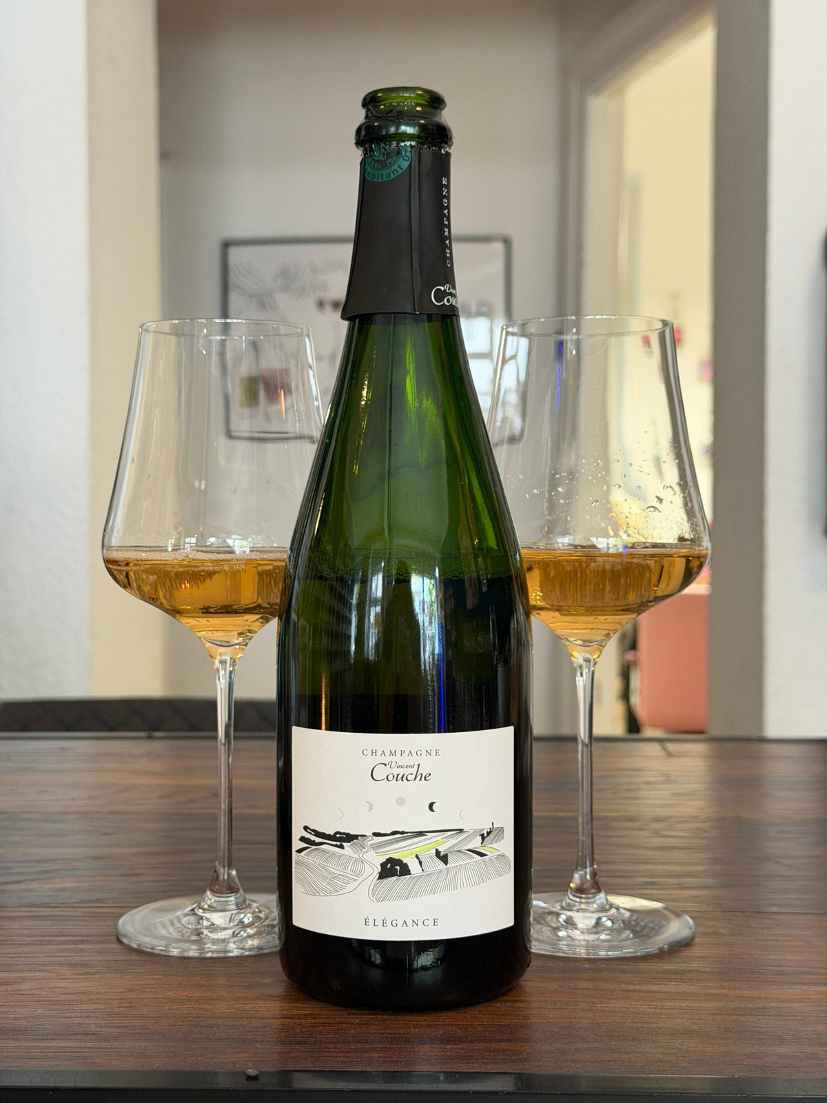 Bottle of Vincent Couche Champagne Élégance Brut Nature with two filled glasses on a wooden table
